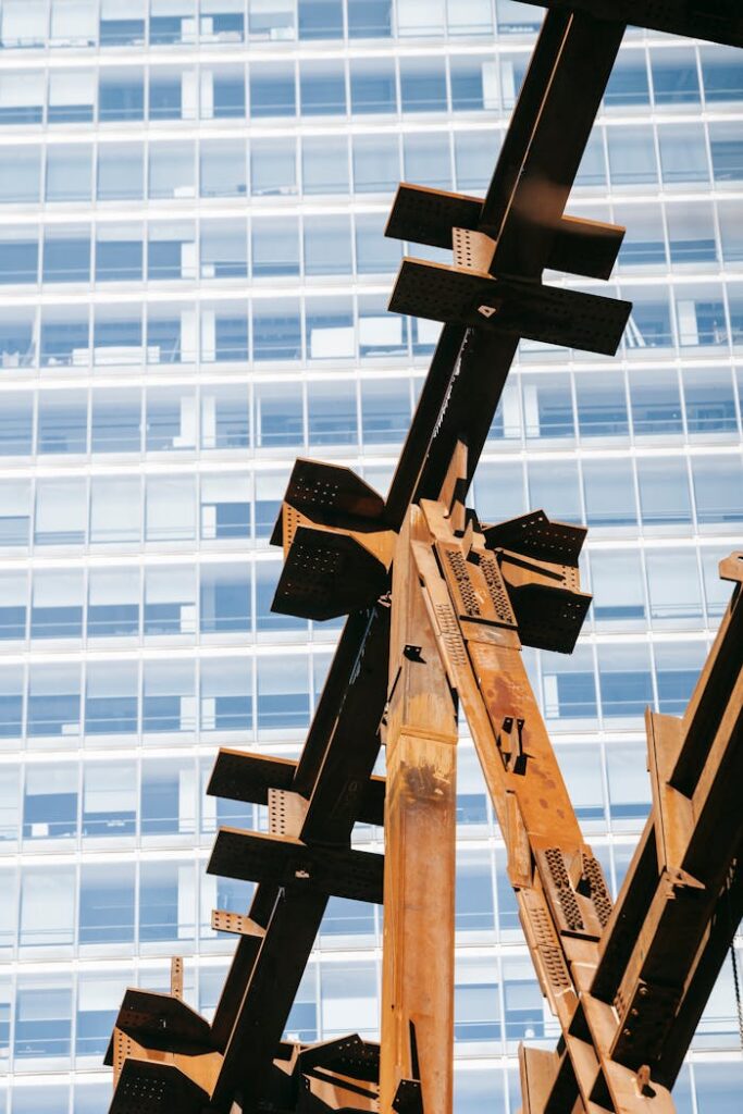 Low angle of rusty metal part of building under construction against office tower in developing district